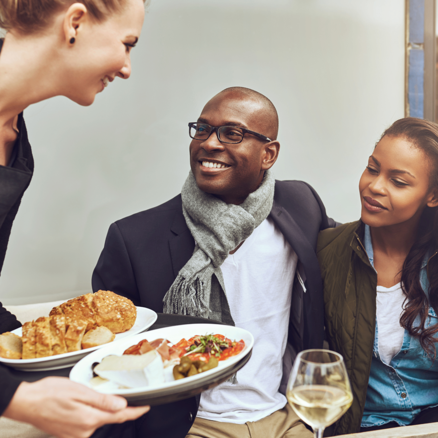 A server presenting a charcuterie board to a smiling couple at a restaurant